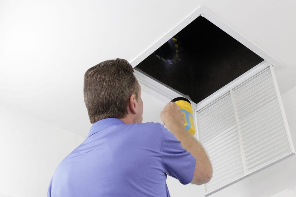 Homme inspectant un conduit d'air avec une lampe de poche.