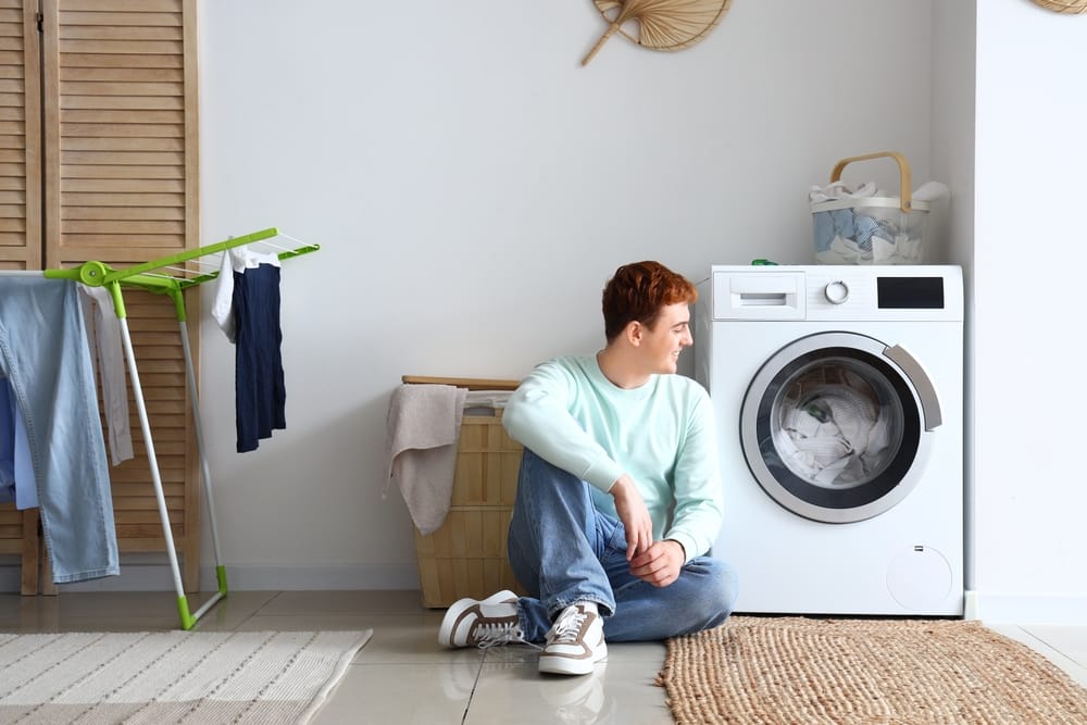 jeune homme assis près de la machine à laver à la maison